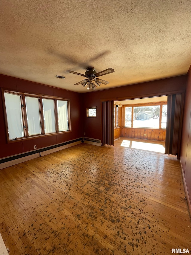 interior space with visible vents, baseboard heating, ceiling fan, a textured ceiling, and wood finished floors