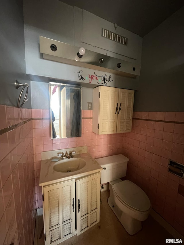 half bath with toilet, a wainscoted wall, vanity, and tile walls