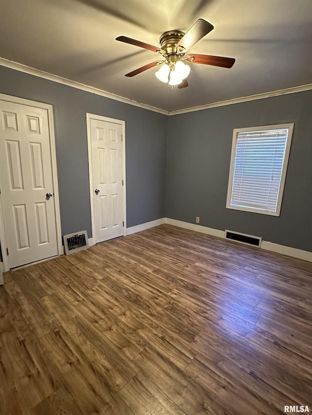 unfurnished bedroom with baseboards, visible vents, dark wood-type flooring, and ornamental molding