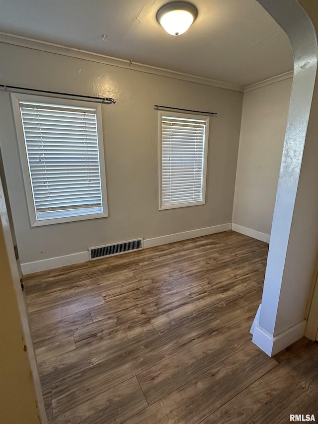 unfurnished room with arched walkways, dark wood-style flooring, crown molding, visible vents, and baseboards