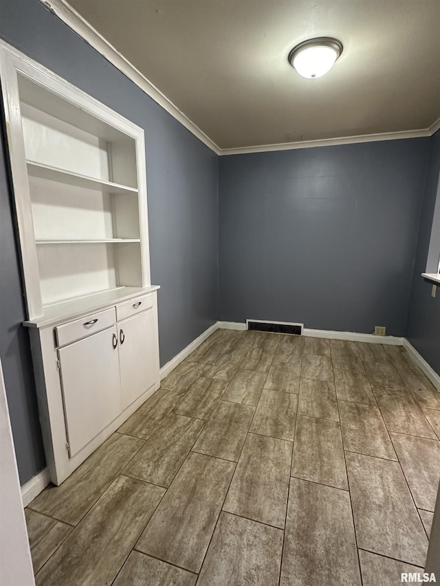 empty room featuring baseboards, visible vents, and crown molding