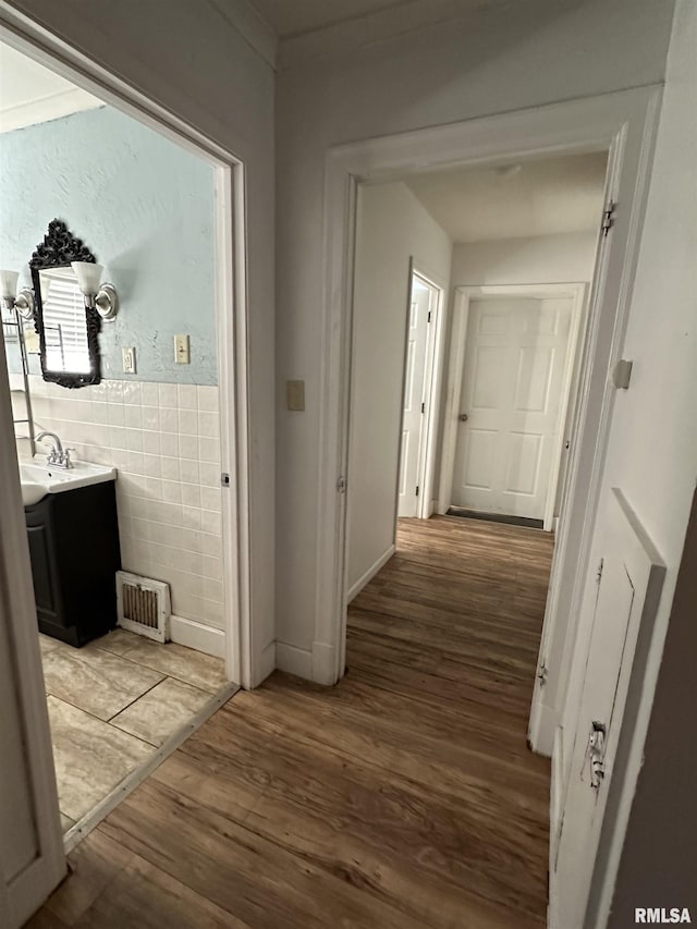 corridor with light wood-style floors, visible vents, a sink, and tile walls