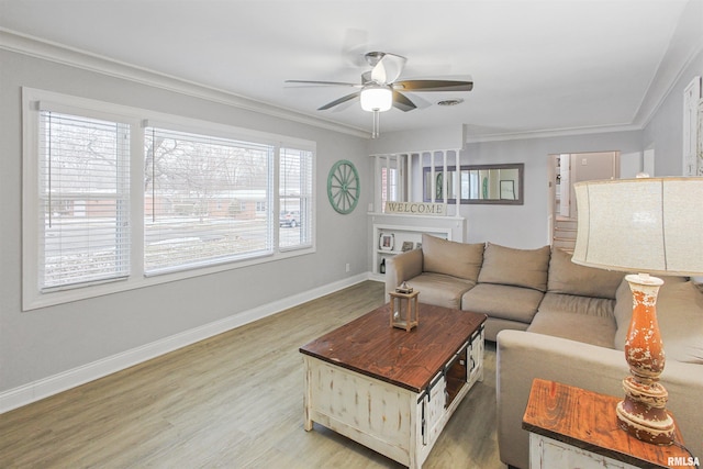 living room featuring ceiling fan, visible vents, baseboards, light wood-style floors, and ornamental molding