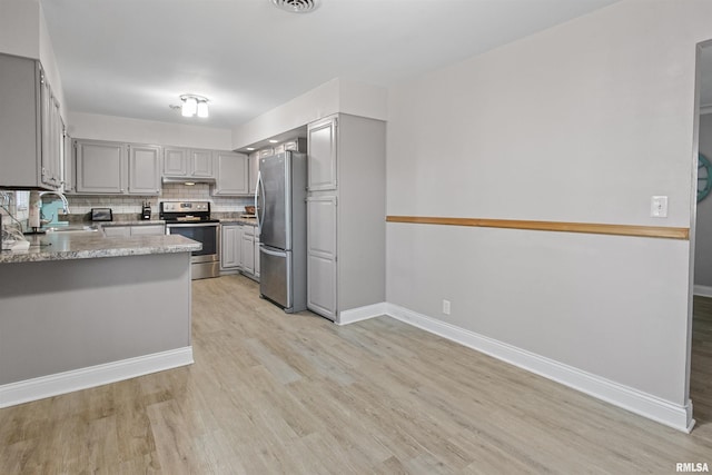 kitchen featuring light wood finished floors, tasteful backsplash, appliances with stainless steel finishes, gray cabinetry, and a sink