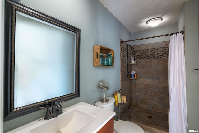 bathroom featuring vanity, toilet, a tile shower, and a textured ceiling