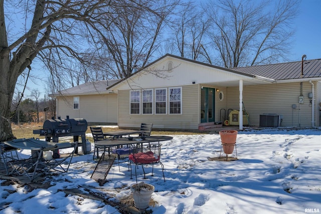 snow covered back of property featuring central air condition unit and metal roof