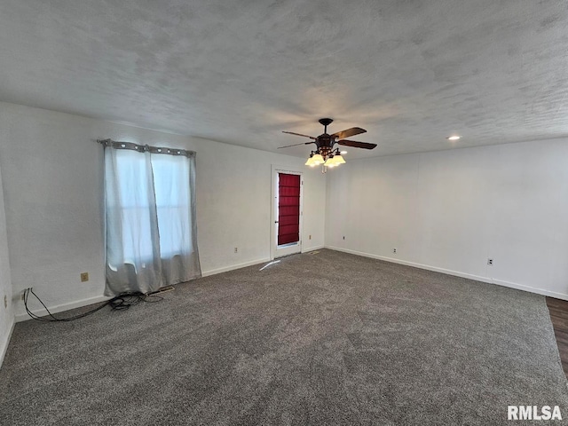 empty room featuring a textured ceiling, dark colored carpet, ceiling fan, and baseboards