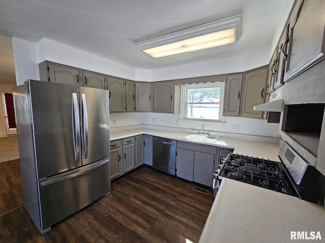 kitchen featuring under cabinet range hood, dark wood-type flooring, a sink, appliances with stainless steel finishes, and gray cabinets