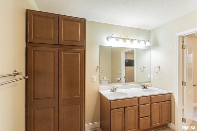 bathroom featuring double vanity, baseboards, toilet, and a sink