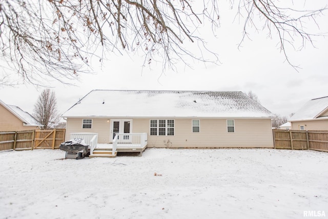 snow covered back of property with a fenced backyard and a wooden deck