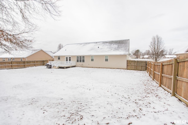 snow covered back of property with a fenced backyard and a deck