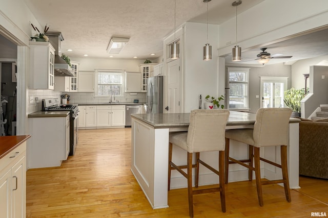 kitchen featuring decorative backsplash, glass insert cabinets, appliances with stainless steel finishes, white cabinetry, and light wood-type flooring