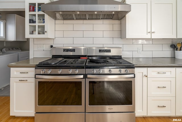 kitchen featuring wall chimney range hood, stainless steel gas range, glass insert cabinets, and washing machine and dryer