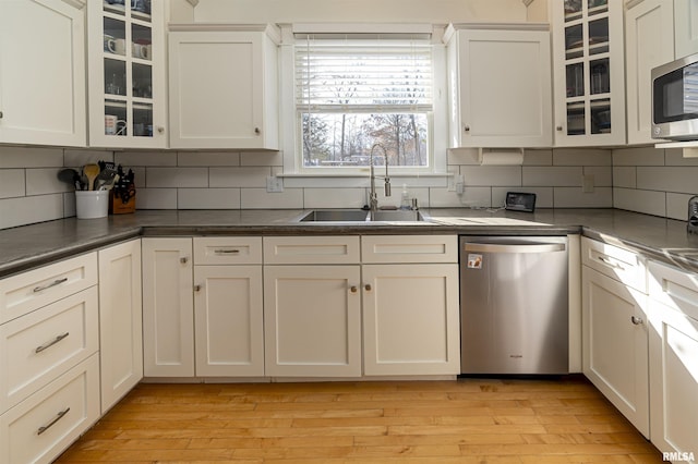 kitchen with dark countertops, glass insert cabinets, stainless steel appliances, light wood-type flooring, and a sink