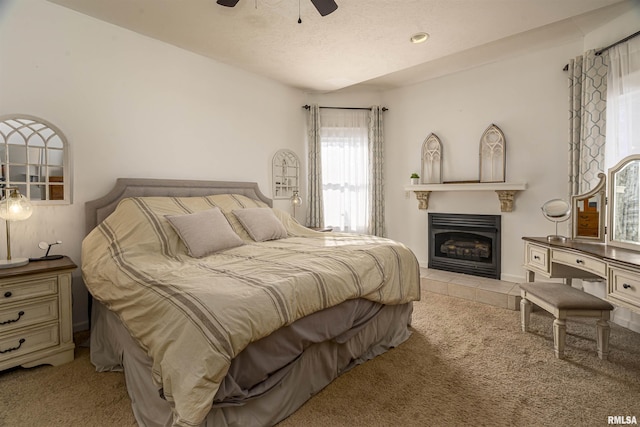 bedroom with a tile fireplace, light colored carpet, ceiling fan, and a textured ceiling