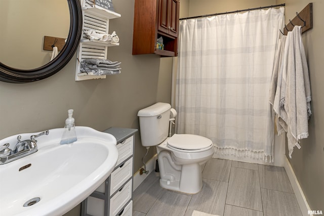 bathroom featuring toilet, baseboards, a sink, and a shower with shower curtain