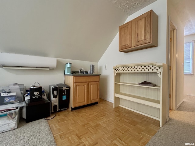 kitchen featuring lofted ceiling, an AC wall unit, brown cabinetry, and baseboards