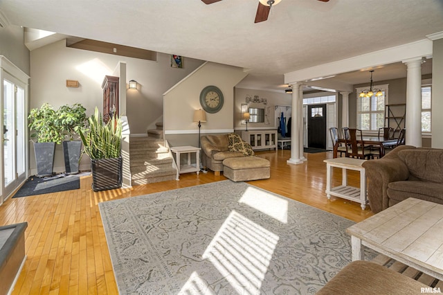 living room with stairs, ceiling fan with notable chandelier, ornate columns, and wood finished floors