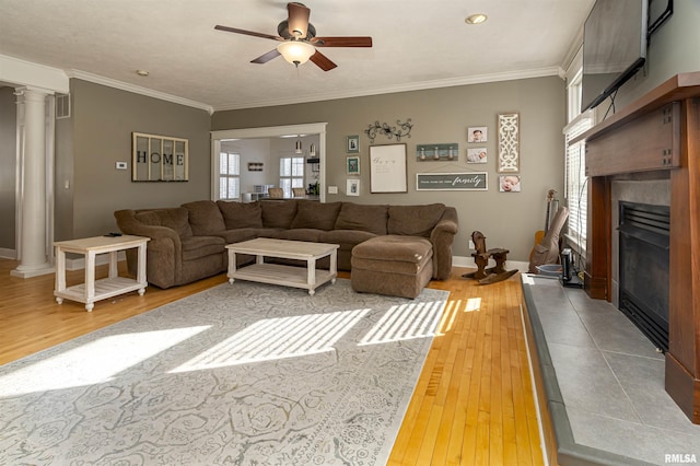 living area with light wood-style floors, baseboards, ornamental molding, a glass covered fireplace, and ornate columns