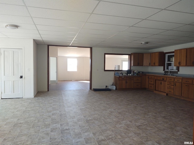 kitchen with a paneled ceiling, baseboards, open floor plan, brown cabinets, and dark countertops