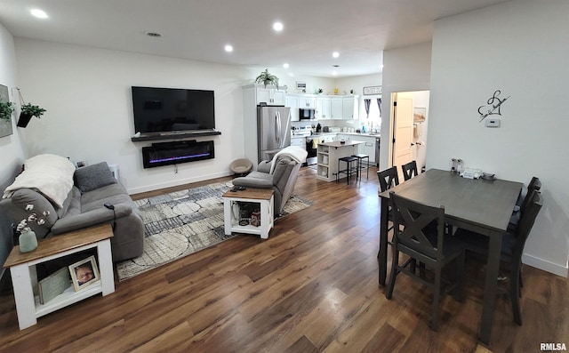 living area featuring dark wood-type flooring, a glass covered fireplace, baseboards, and recessed lighting