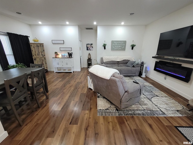 living area with recessed lighting, dark wood finished floors, baseboards, visible vents, and a glass covered fireplace