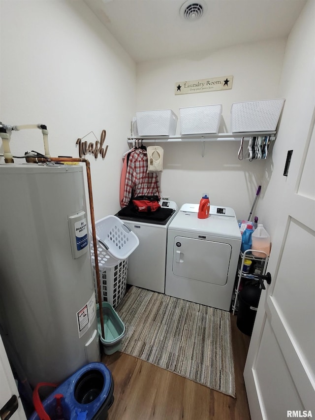 clothes washing area featuring visible vents, electric water heater, wood finished floors, washer and dryer, and laundry area