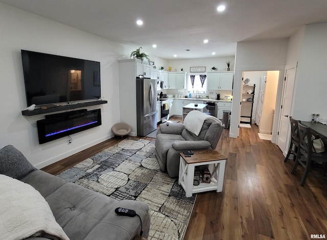 living area with dark wood-style floors, baseboards, a glass covered fireplace, and recessed lighting