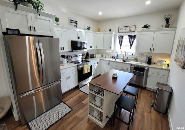 kitchen with dark wood-type flooring, appliances with stainless steel finishes, white cabinets, and a sink