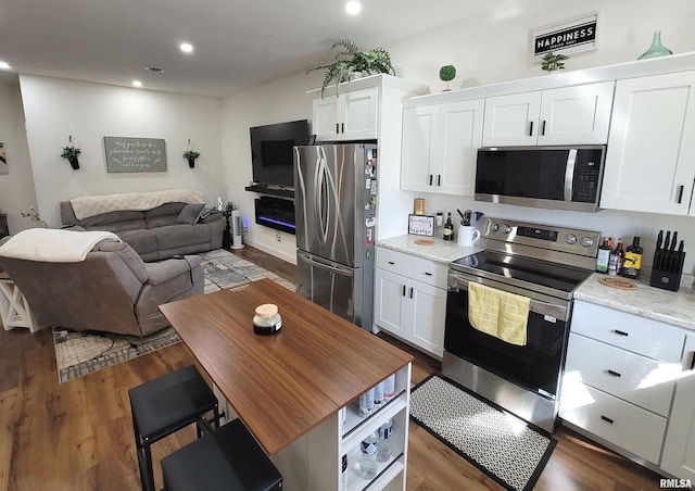 kitchen featuring light stone counters, stainless steel appliances, dark wood-type flooring, white cabinetry, and open floor plan