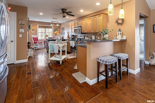 kitchen featuring dark wood-style floors, dark countertops, appliances with stainless steel finishes, a peninsula, and a kitchen breakfast bar