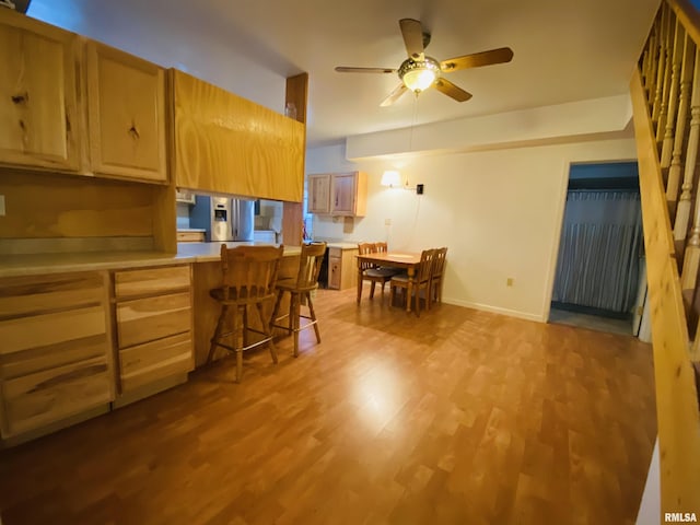 kitchen featuring ceiling fan, light wood-style floors, a kitchen breakfast bar, light countertops, and stainless steel fridge with ice dispenser