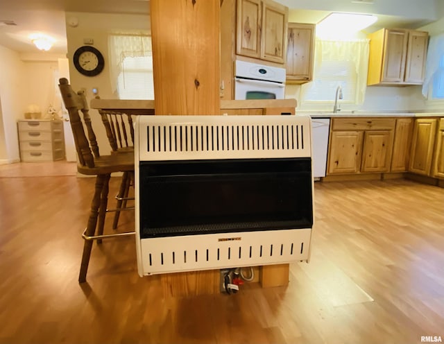 kitchen with light wood-type flooring, white appliances, a sink, and heating unit