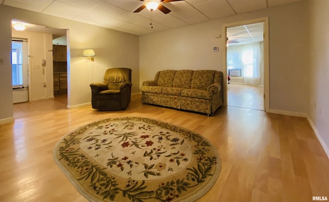 living area with a ceiling fan, a paneled ceiling, baseboards, and wood finished floors