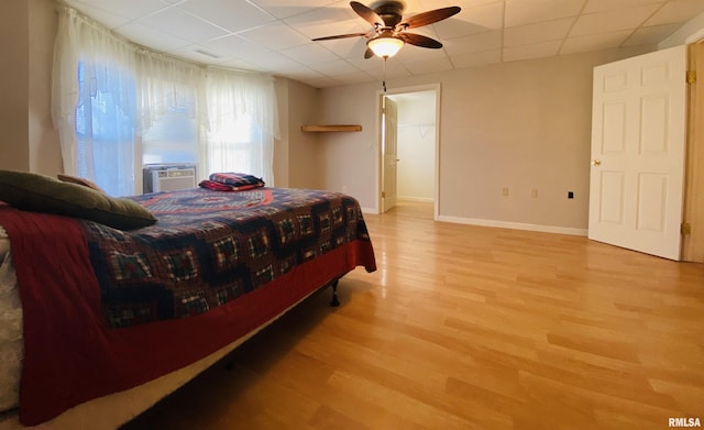 bedroom featuring a drop ceiling, cooling unit, a ceiling fan, baseboards, and light wood finished floors