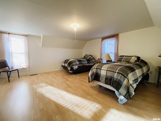 bedroom featuring baseboards, visible vents, vaulted ceiling, and wood finished floors