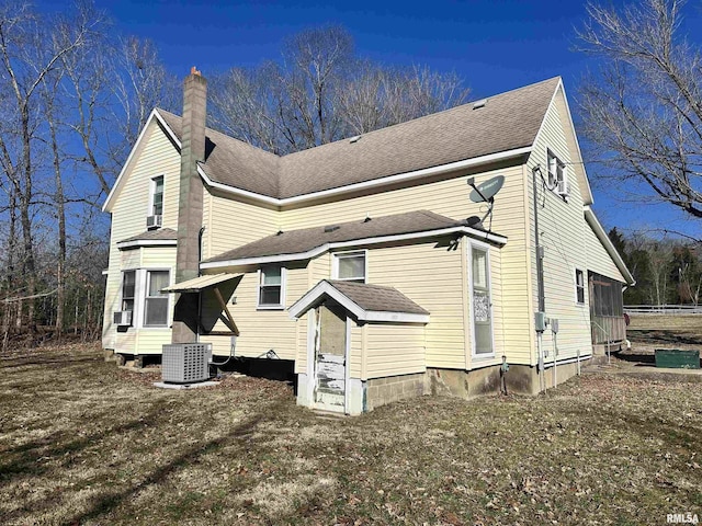 view of side of home featuring a yard, a shingled roof, a chimney, and cooling unit