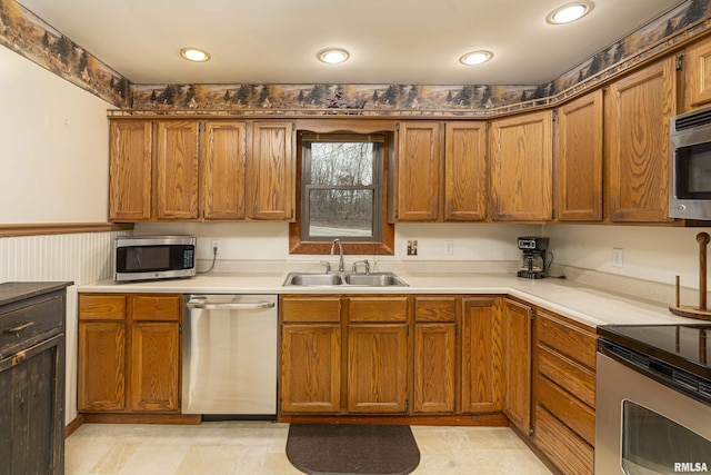 kitchen featuring brown cabinetry, stainless steel appliances, light countertops, a sink, and recessed lighting