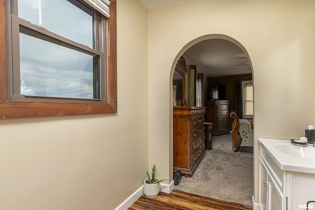 hall featuring carpet floors, baseboards, arched walkways, and a sink