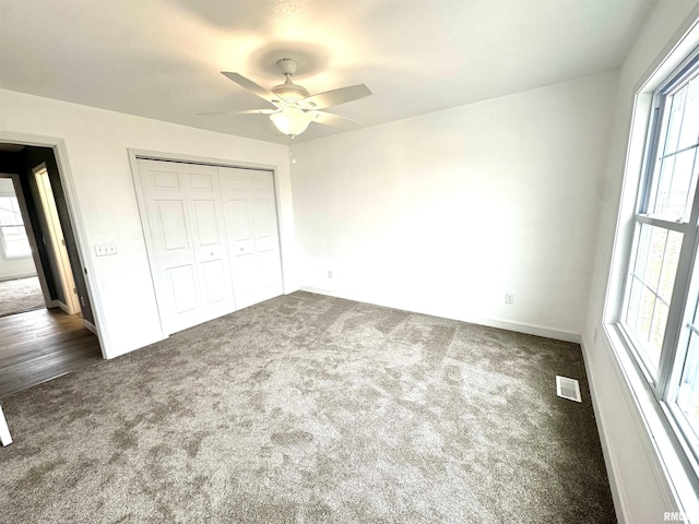 unfurnished bedroom with multiple windows, dark carpet, a closet, and visible vents