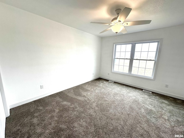 spare room featuring visible vents, dark colored carpet, a ceiling fan, and baseboards