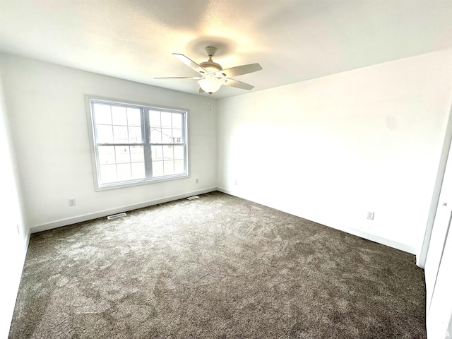 unfurnished room featuring baseboards, visible vents, dark carpet, and a ceiling fan