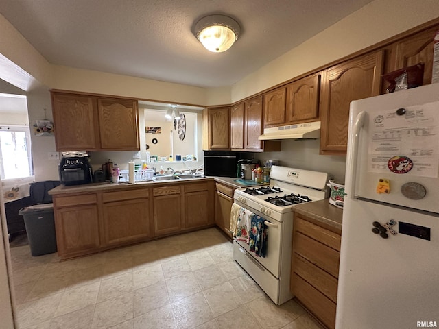 kitchen featuring white appliances, under cabinet range hood, brown cabinetry, and a sink