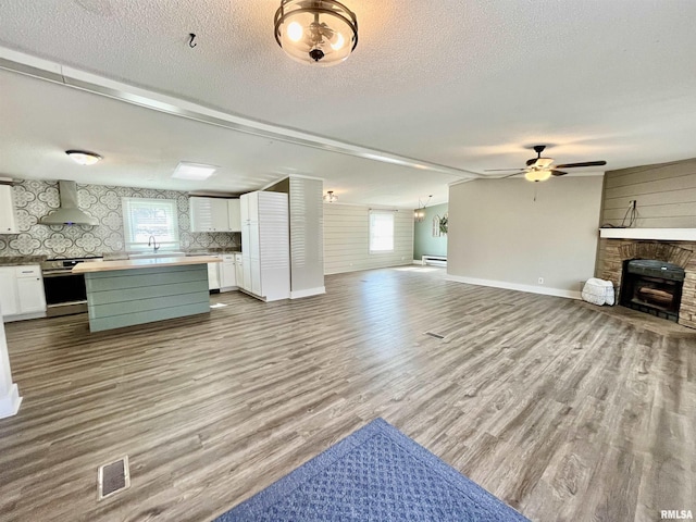 unfurnished living room featuring a fireplace, visible vents, a baseboard heating unit, a textured ceiling, and wood finished floors