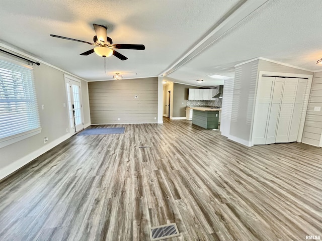 unfurnished living room with lofted ceiling, visible vents, a textured ceiling, wood finished floors, and baseboards