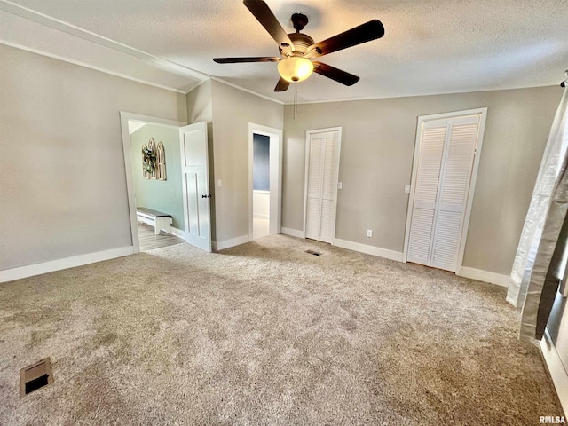 unfurnished bedroom featuring multiple closets, carpet flooring, a textured ceiling, and baseboards