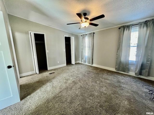 unfurnished bedroom featuring lofted ceiling, a textured ceiling, visible vents, carpet, and two closets