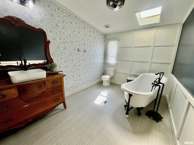 full bathroom featuring toilet, a decorative wall, vanity, a soaking tub, and wallpapered walls