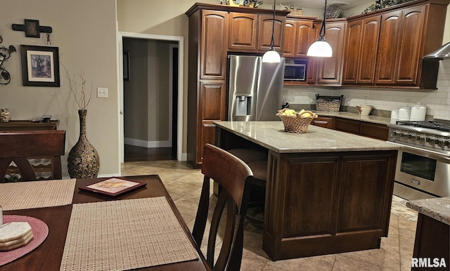 kitchen with a kitchen island, appliances with stainless steel finishes, hanging light fixtures, wall chimney range hood, and backsplash