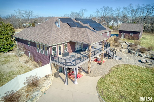 exterior space featuring driveway, solar panels, roof with shingles, an outdoor structure, and a front lawn